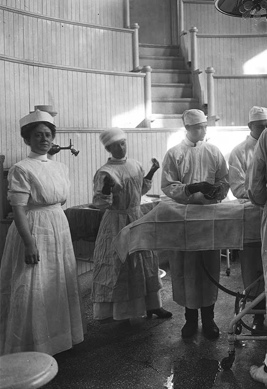 Operating room scene, 1913. To the far left is Tabitha Grier, RN, operating room nurse supervisor, who graduated from the U.Va. nursing program in 1912 and served as superintendent from 1913 to 1916.  Surgical Amphitheater, University of Virginia Hospital, 1913-02-08, Hollsinger Collection, Albert and Shirley Small Special Collections Library, University of Virginia