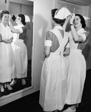 A 1954 second-year student admires the new black band on her cap, adjusted by a classmate.	Mildred Corum (later Campbell), BSN 1956, adjusts the cap of June Finlay (later Cain), BSN 1954. Eleanor Crowder Bjoring Center for Nursing Historical Inquiry, University of Virginia School of Nursing.
