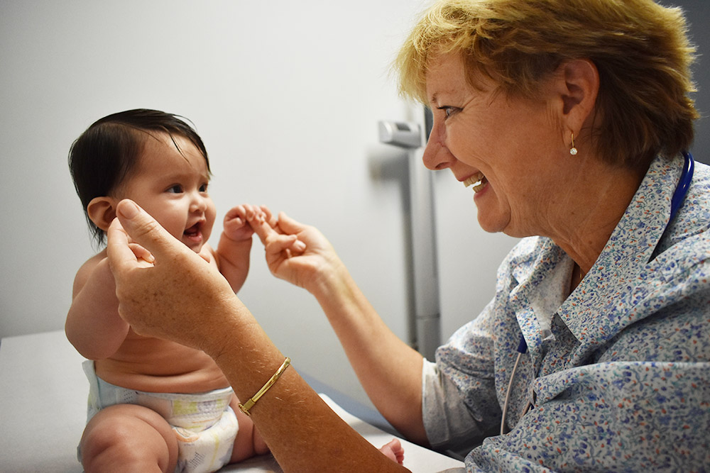An image of a nurse practitioner smiling at an infant in a clinic setting.
