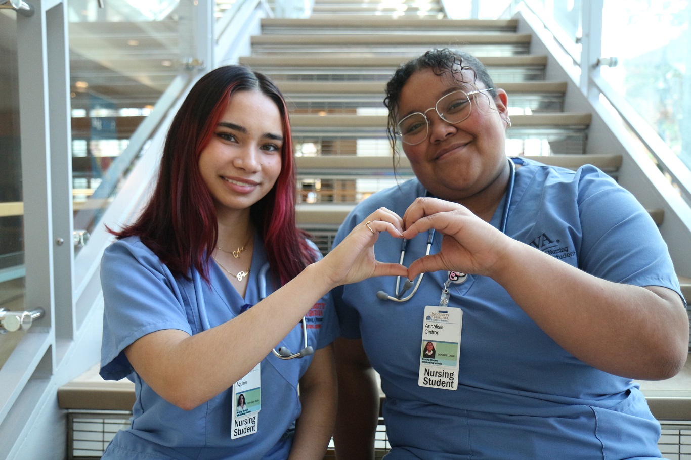 Two nursing students sitting on the steps, forming a heart shape with their hands.