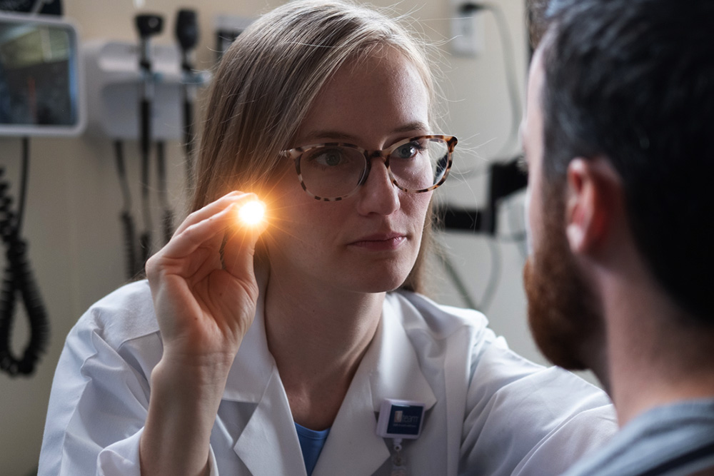 Prof. Jessie Gibson, a nursing professor who studies Huntington's disease, shines a light into a patient's eyes during a physical exam.
