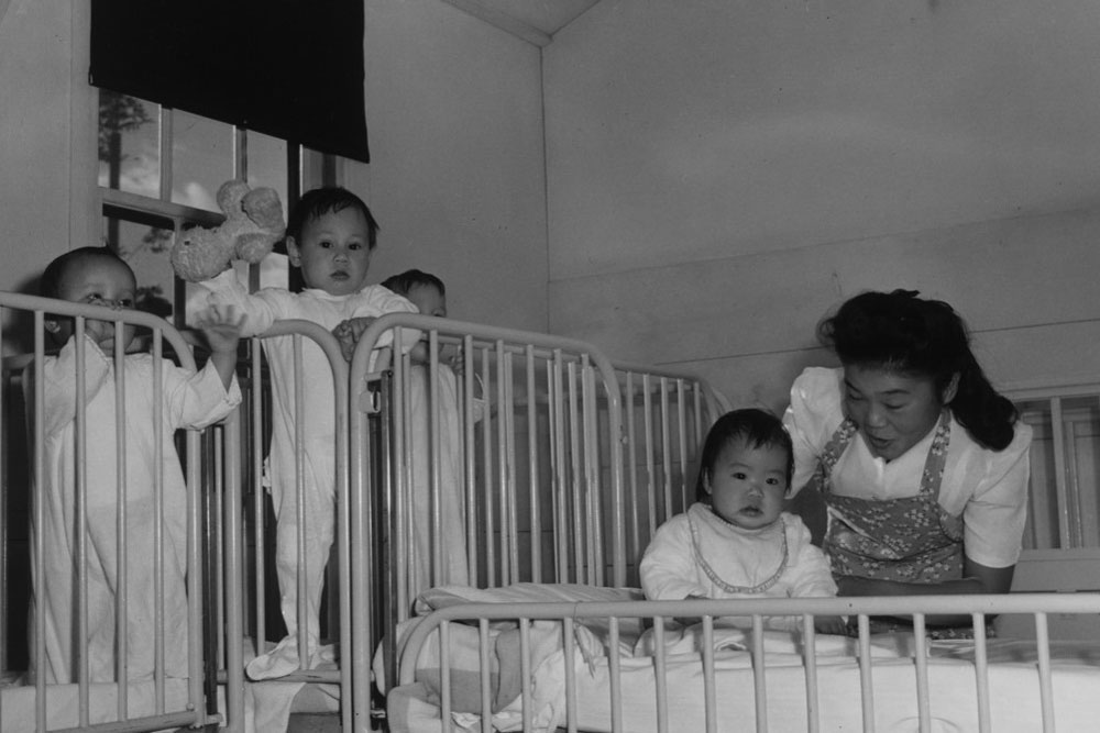 A nurse's aide at Manzanar with detained children and infants, c. 1943.
