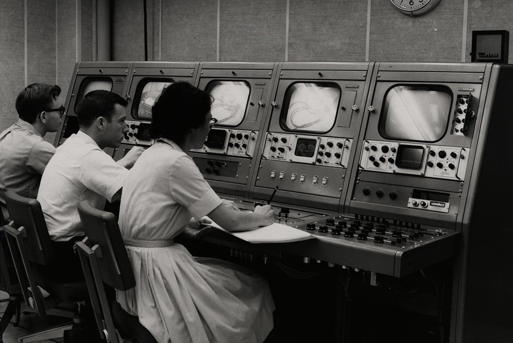 a nurse and technicians sit at a row of monitors during video recording