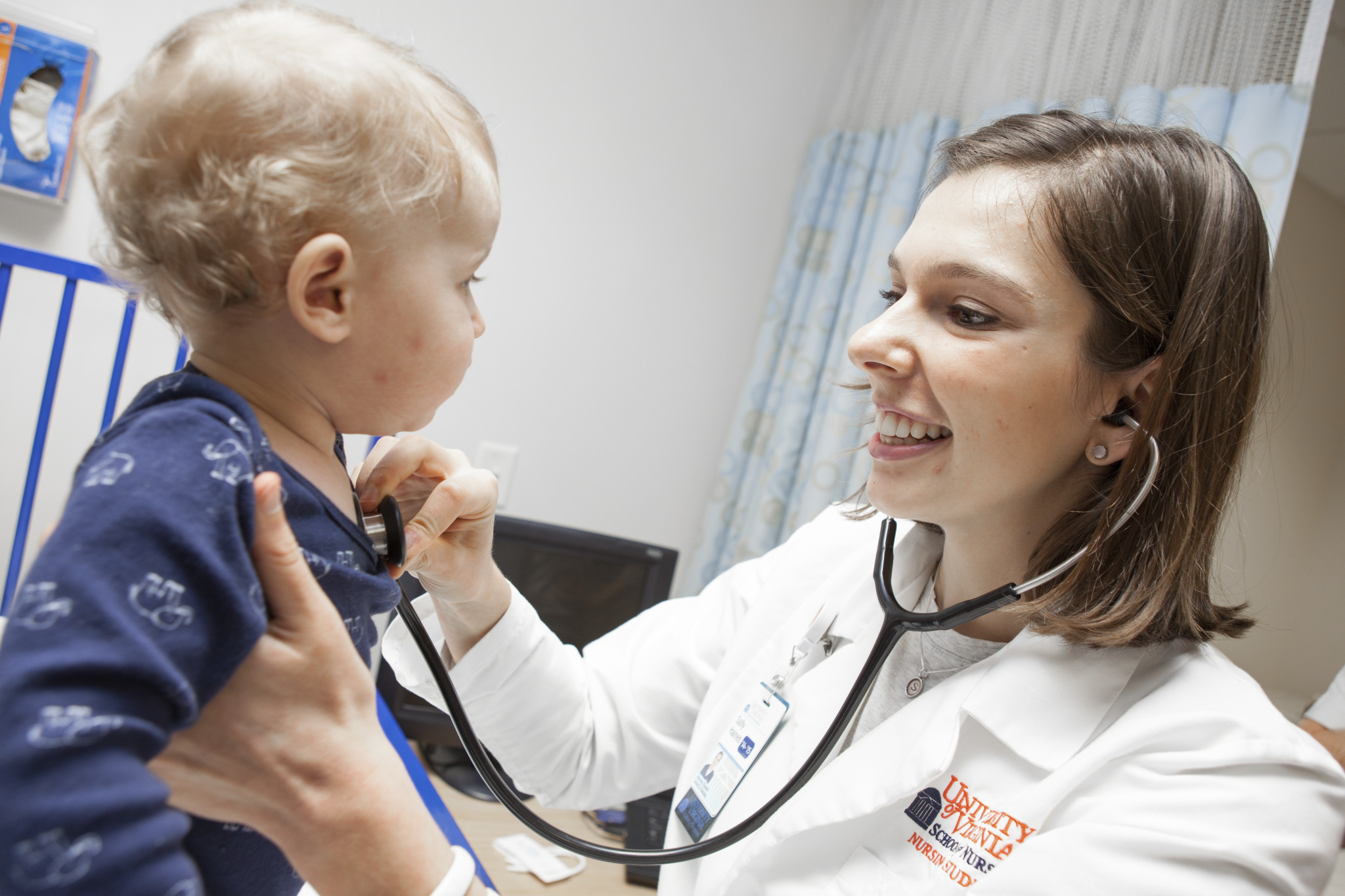 An image of a nurse practitioner assessing a small child with her stethoscope in a clinic setting.