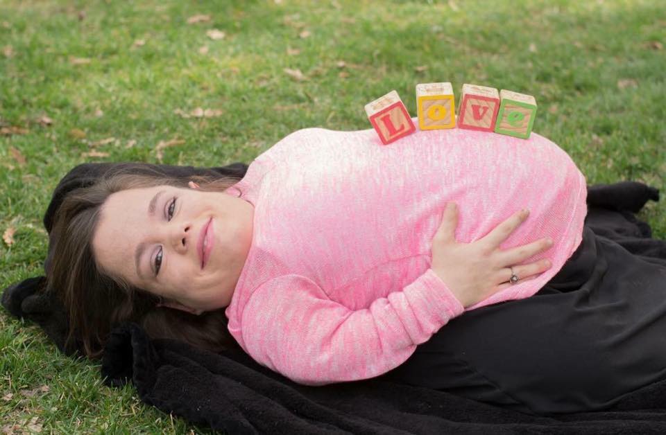 Pregnant woman lying on her back with wooden alphabet blocks atop her stomach spelling L-O-V-E