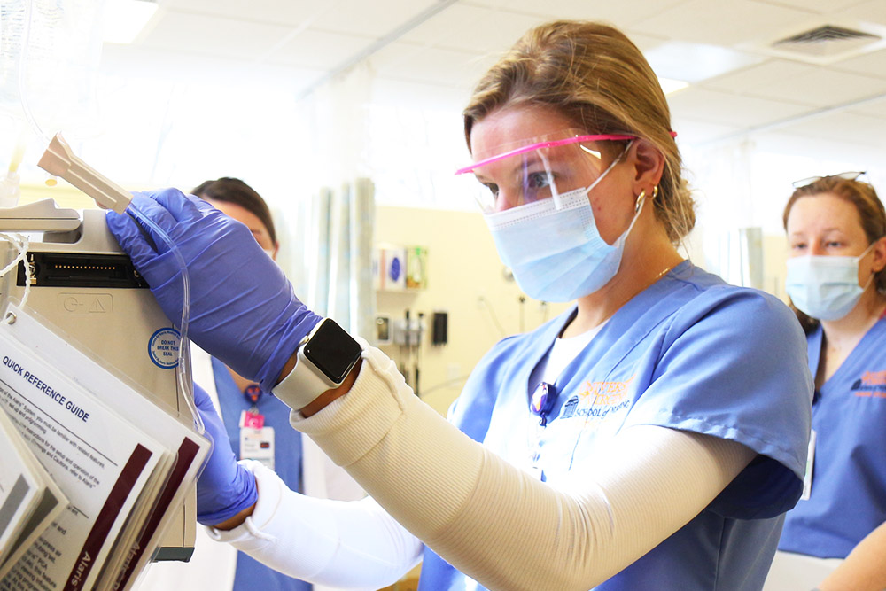 An image of a BSN student wearing a mask and gloves checking an IV pump in the sim lab