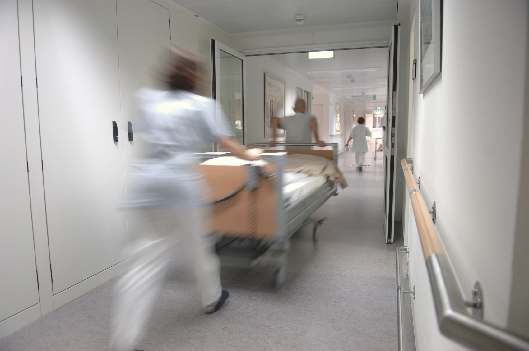 A nurse wheels a patient on a gurney down a hospital corridor.