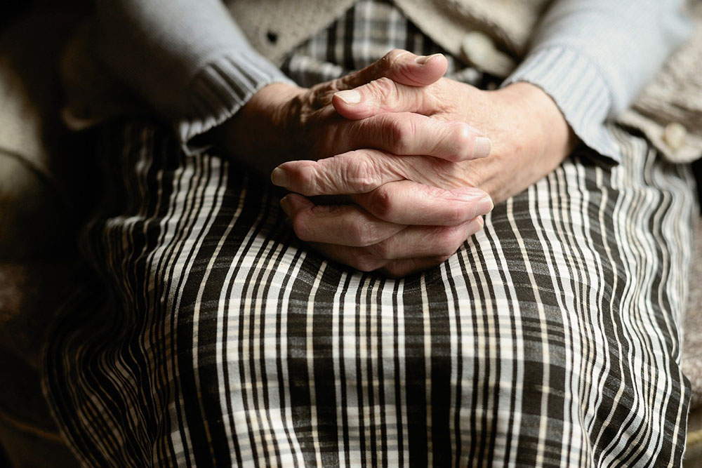 An image of an older woman's hands clasped in her lap.
