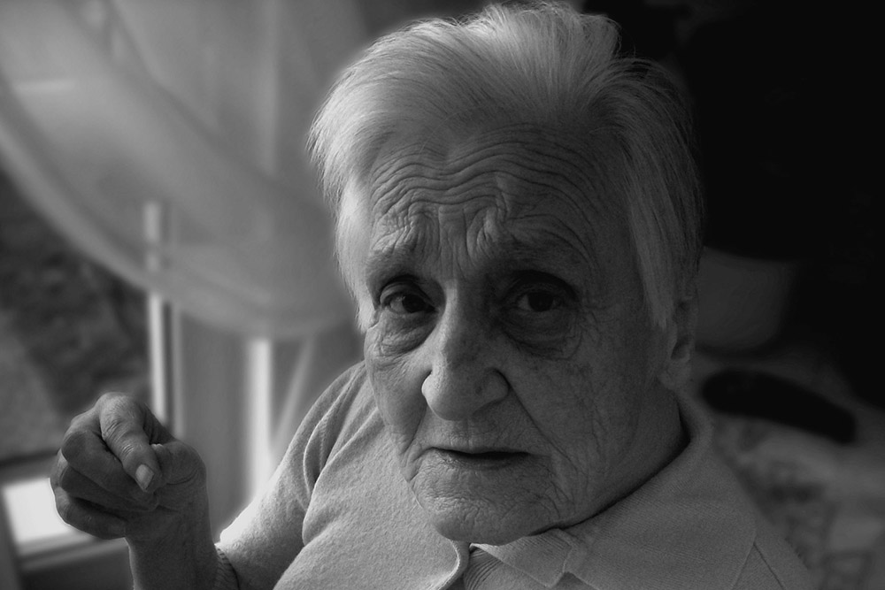 A black and white image of an elderly woman looking at the camera quizzically.