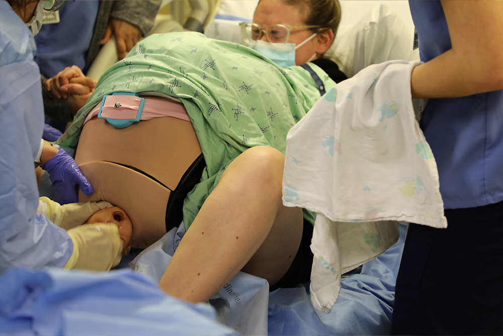 Nursing students observe an actor wearing new simulated birthing tech to prepare for obstetrics clinical rotations.