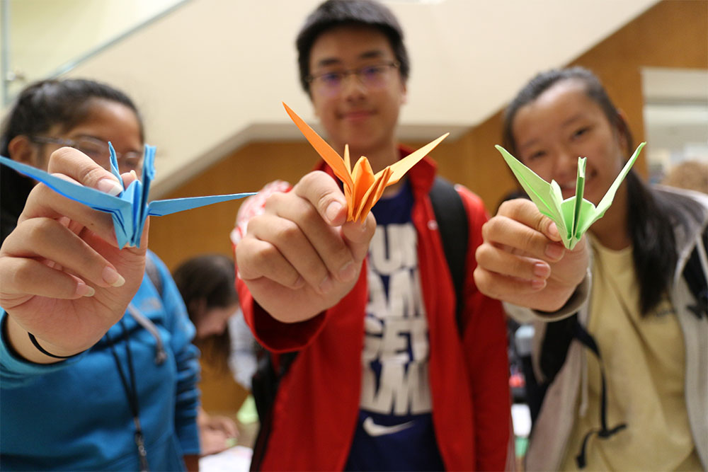 An image of three Asian students taking part in the #HoosInclusive photo campaign and crane folding event in 2019