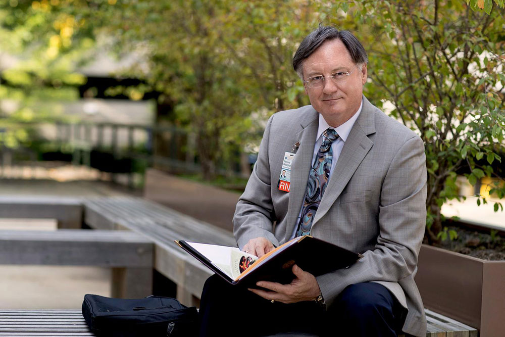 Professor Richard Westphal sits reading a book on a bench outside of the the UVA School of Nursing