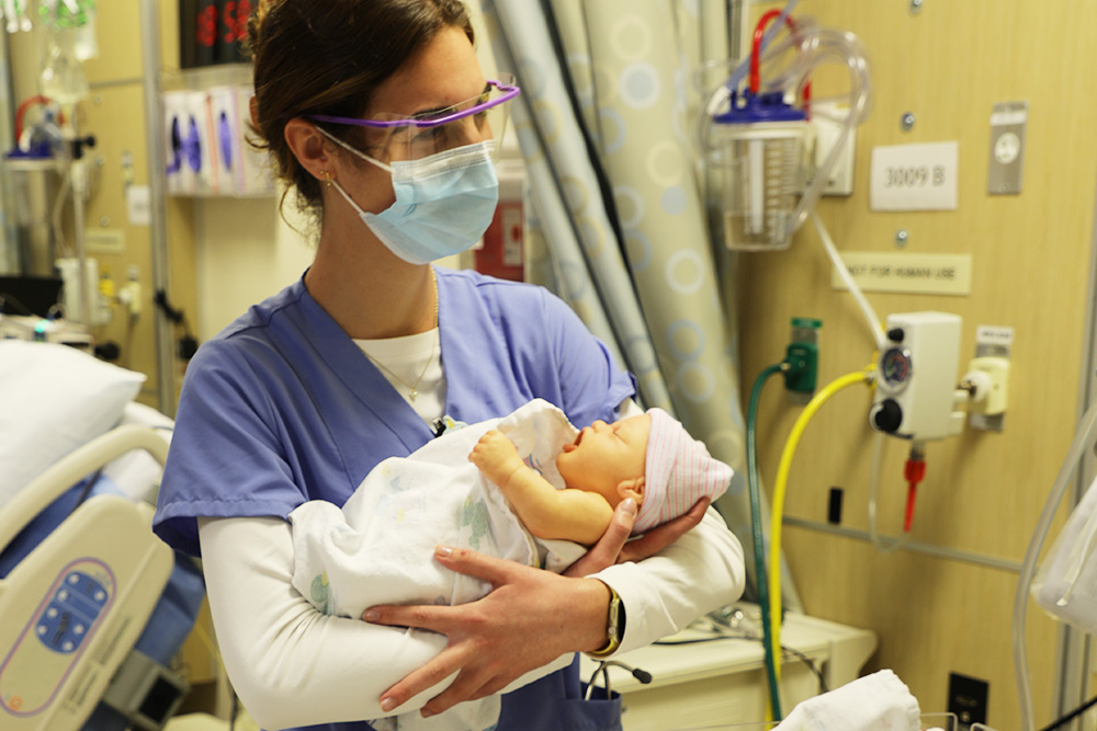 A nursing student holds a simulated baby after an OB sim that uses new tech and a actor standardized patient.